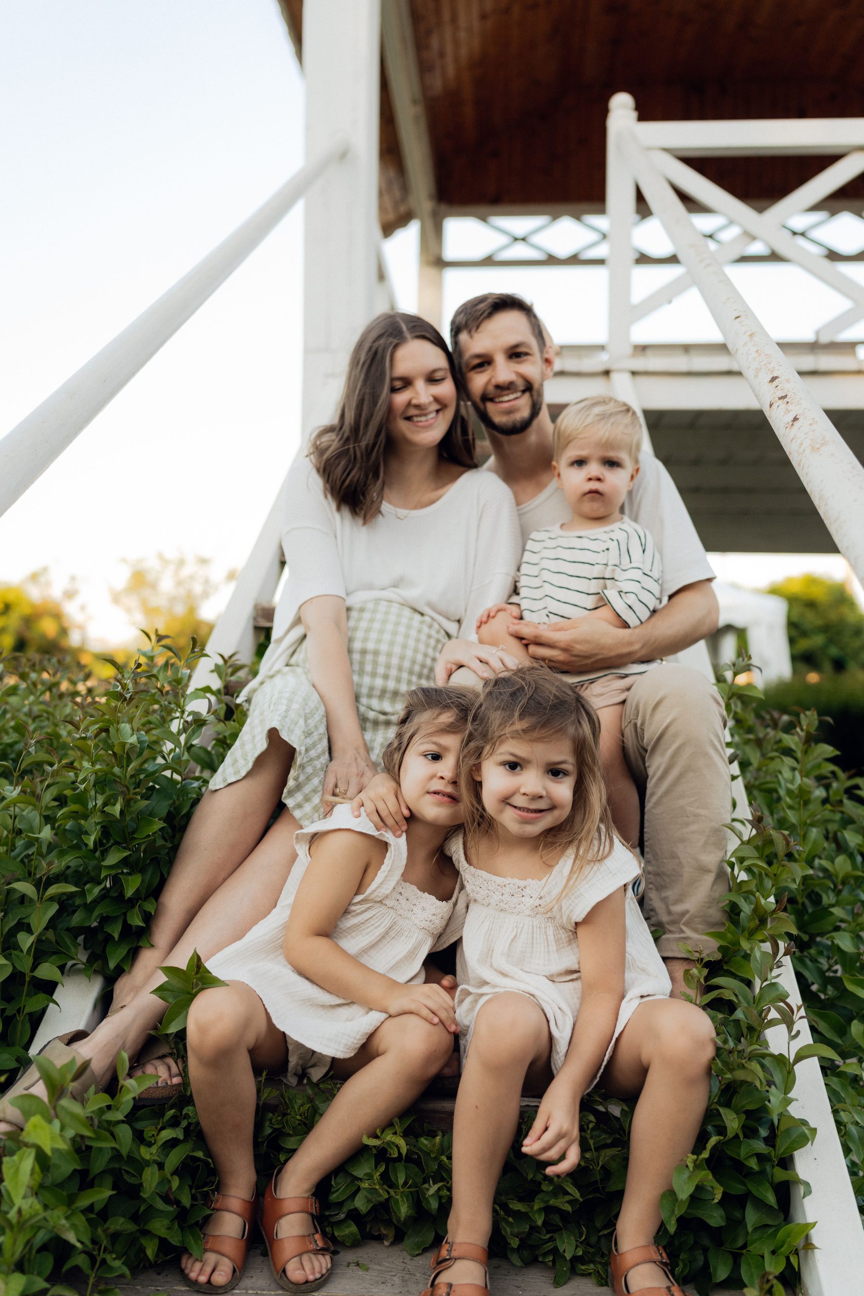 A family of five sitting together on the front steps of a home at sunset